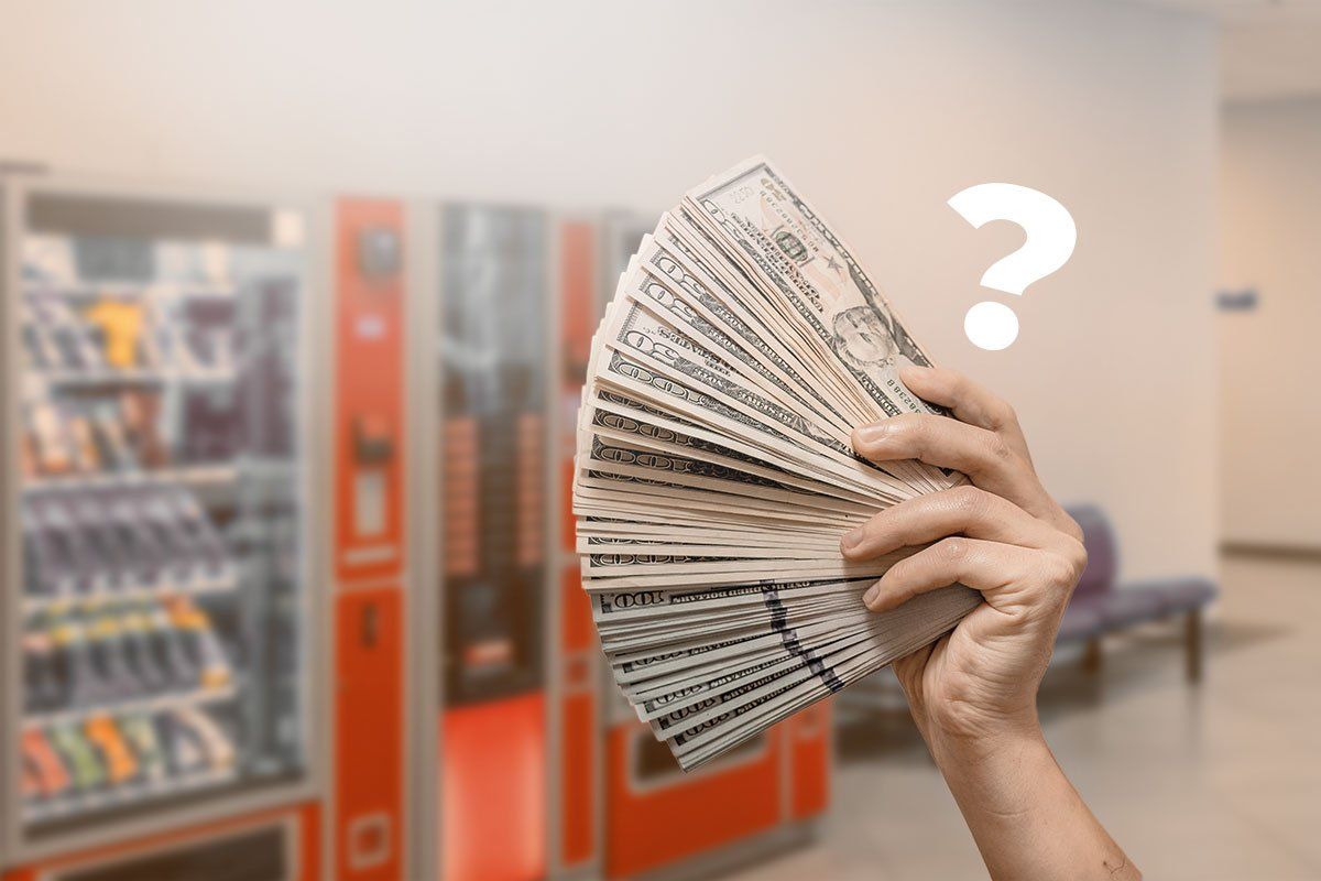 Hand holding fan of cash in front of vending machines placed in a hallway