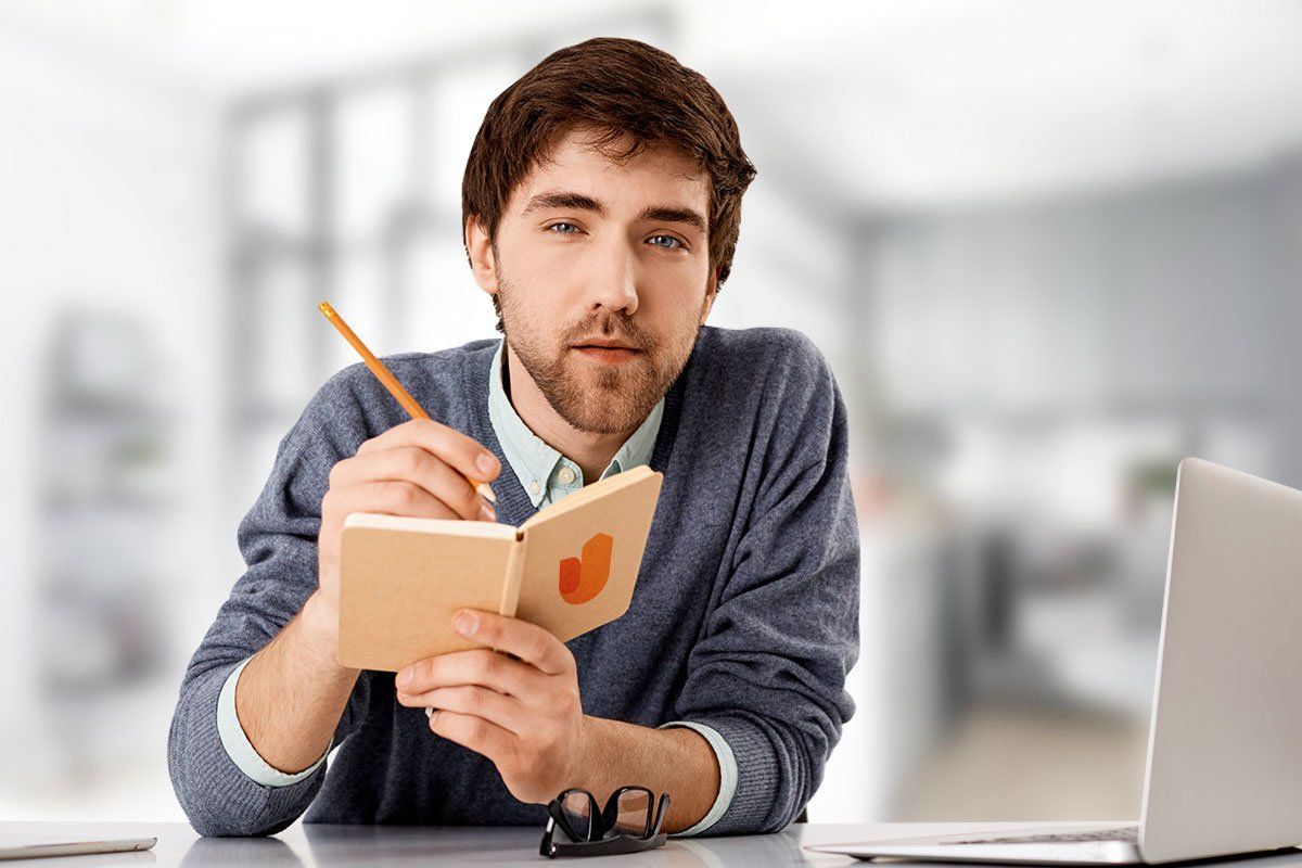 Young business man holding a notebook and pen and looking across desk during a business name brainstorming session